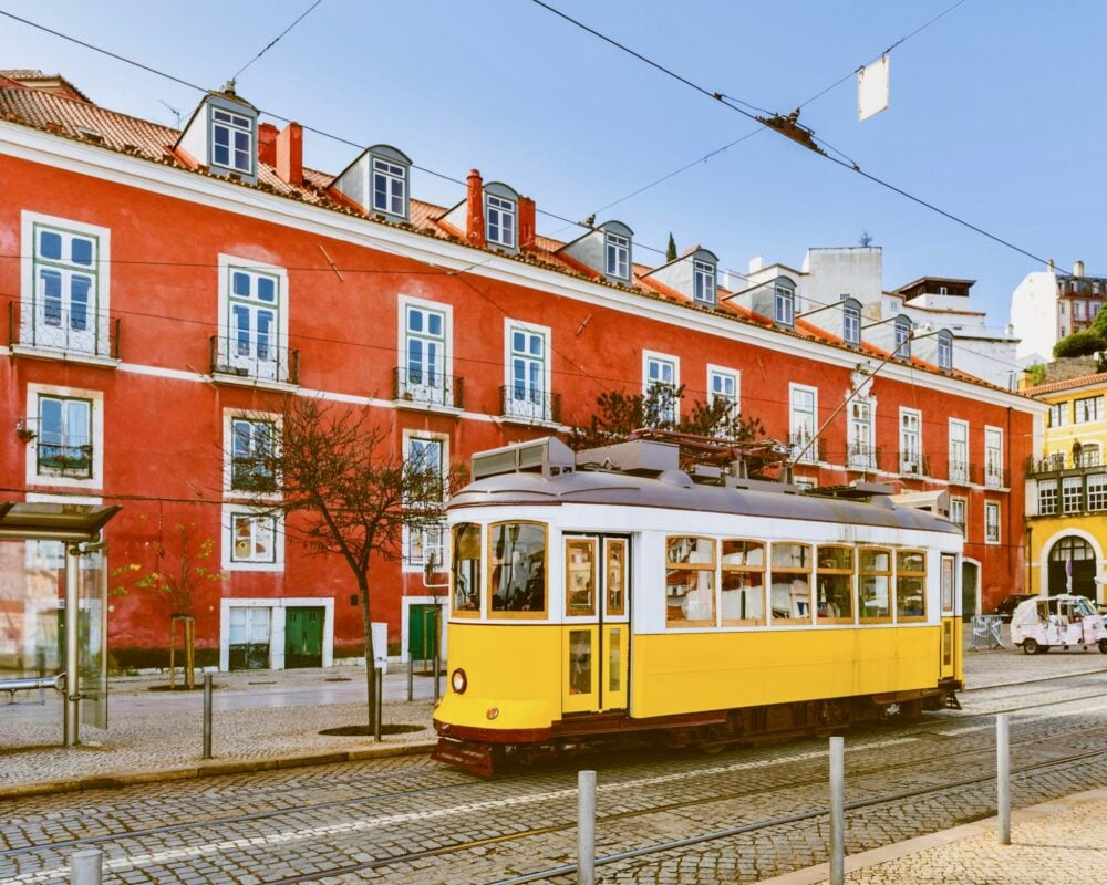 Yellow Tram 28 passing red buildings, one of the best things to do in Lisbon